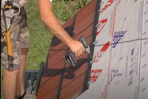 Worker installing wood shakes on a roof with power tool